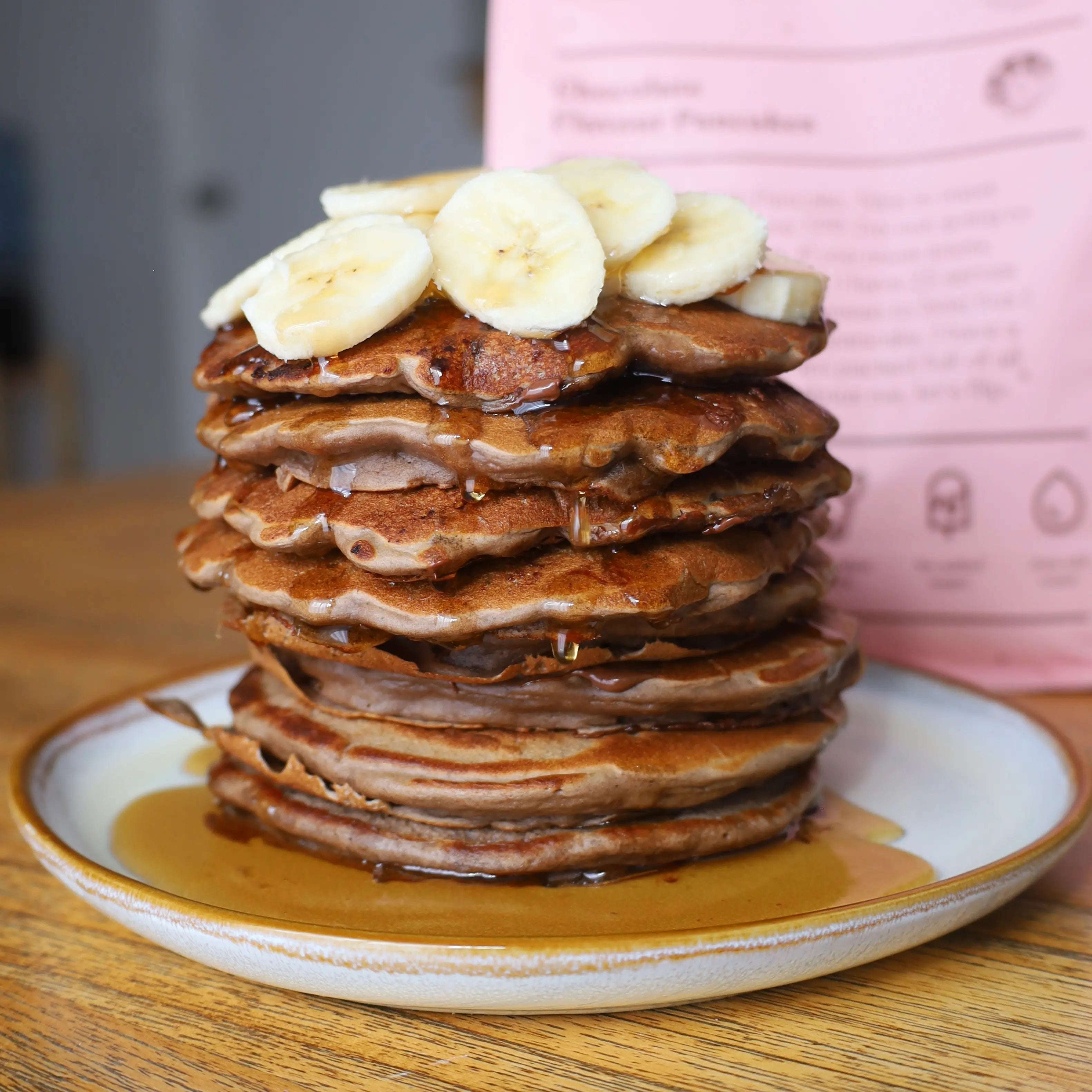 Double Choc Chip Banana Pancakes by the protein pancake pancake with banana on top and maple syrup dripping