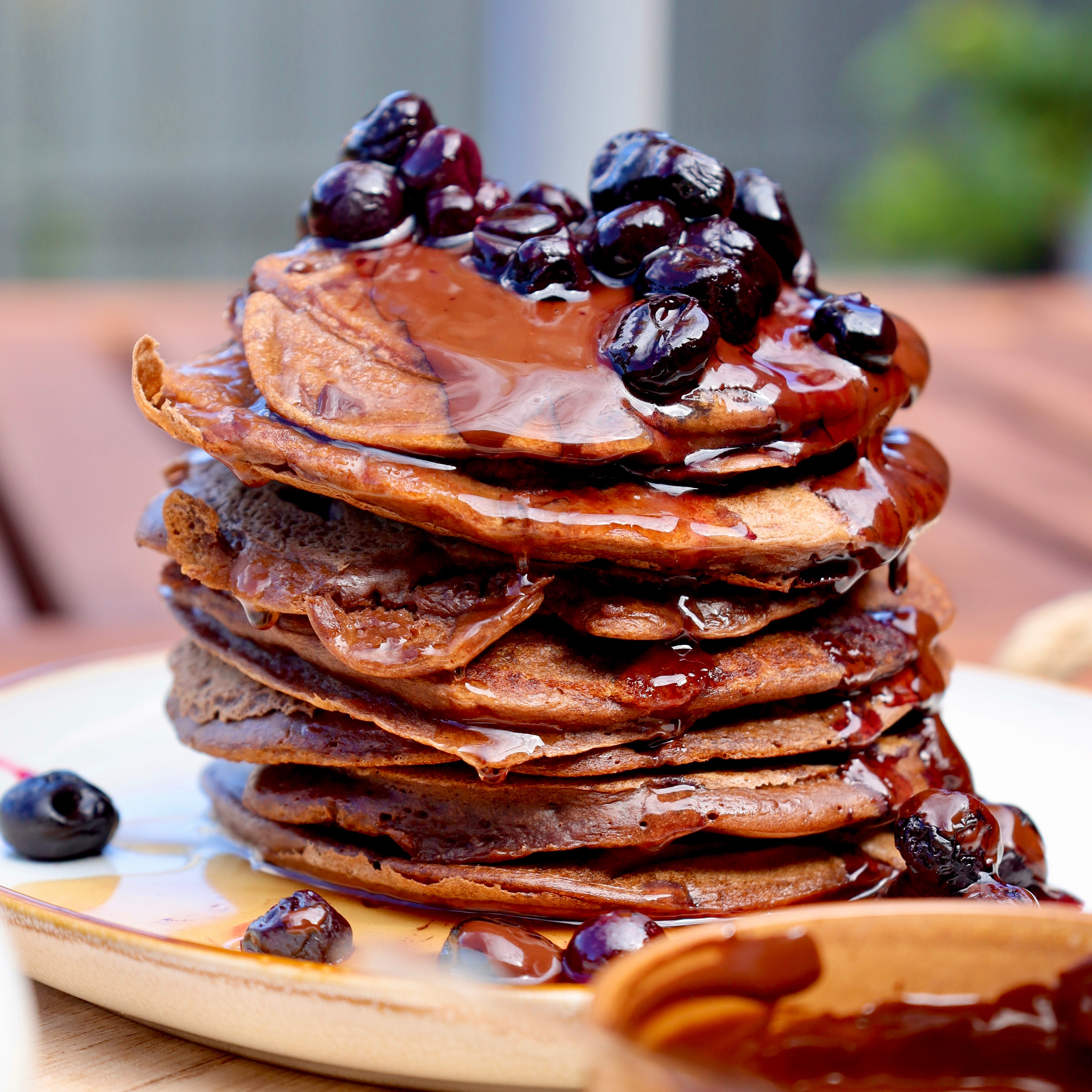 Fluffy chocolate protein pancakes topped with warm blueberry compote, drizzled with melted dark chocolate and maple syrup